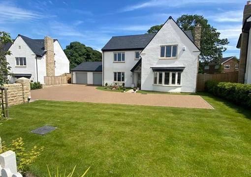 wide image of a property, front garden, plants, resin bound driveway and blue sky